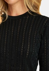 Czarny dzianinowy top z pionowymi paskami i małymi wycięciami, okrągłym dekoltem oraz ribbową struktura. Materiał jest lekki i lekko teksturowany.