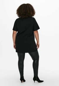 Svart oversized t-shirt med korta ärmar, ihopparad med tighta blanka svarta leggings och klackade svarta ankelstövlar. Enkelt, slätt material.
