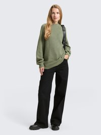 Zelena rebrasta pletena majica z visokim ovratnikom, kombinirana s črnimi širokimi hlačami in črnimi škornji z debelim podplatom. Enostaven, priložnostni dizajn.