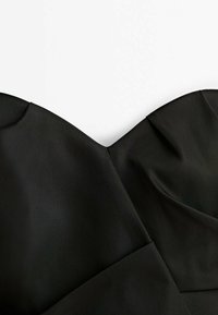 Gros plan sur l'encolure en cœur et le corsage structuré d'une robe bustier noire sur fond blanc.