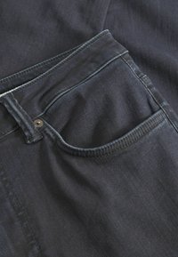 Tamsūs džinsai pasižymi tradicine penkių kišenių konstrukcija su metaline sagtele. Medžiaga turi lygų paviršių su švelniais spalvos variacijomis.