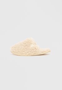 Cremefarvede slippers lavet af tekstureret, fluffy materiale med åben bagside og flad sål. Blød og hyggelig finish.