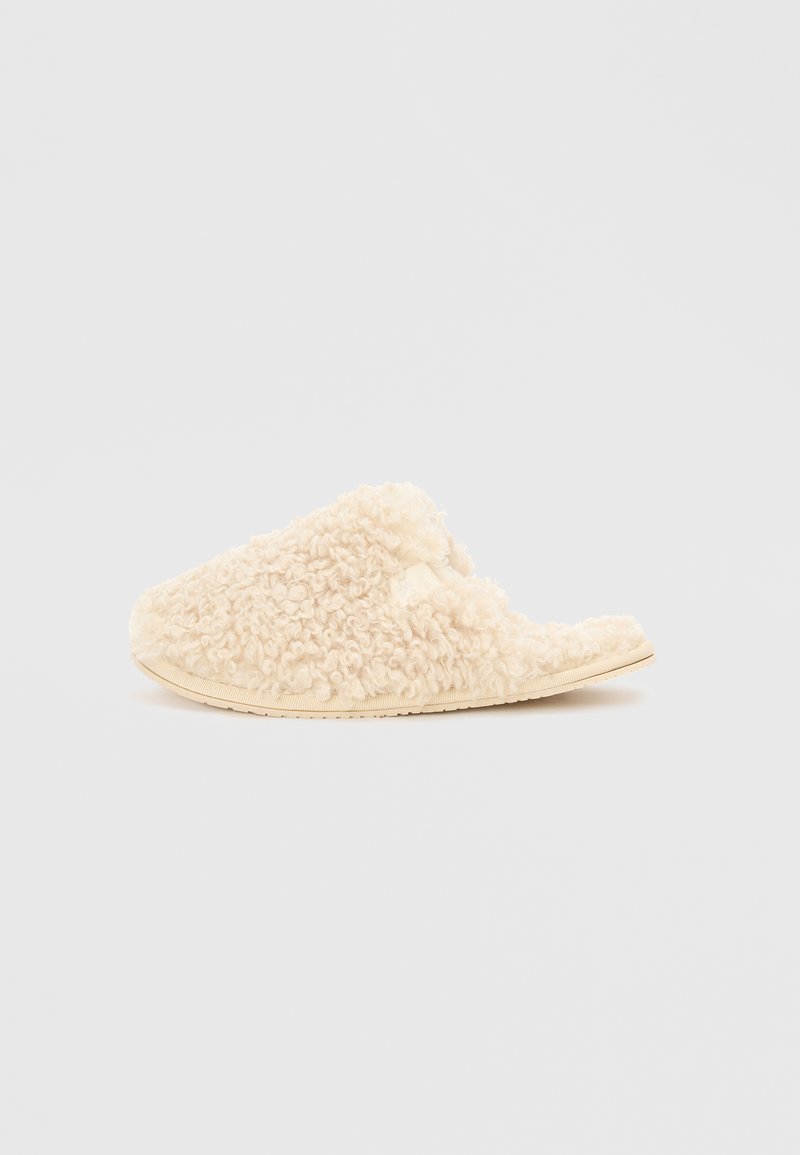Cremefarvede slippers lavet af tekstureret, fluffy materiale med åben bagside og flad sål. Blød og hyggelig finish.