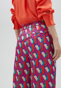 Färgglada mönstrade byxor med geometriska former i rött, rosa, turkos och beige; tillverkade av ett slätt tyg med en skräddarsydd midja.