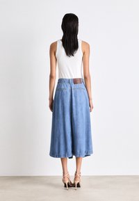 Jupe-culotte en denim bleu clair, avec une taille ornée d'un accent marron texturé, une coupe ample et un ourlet reposant juste au-dessus de la cheville.