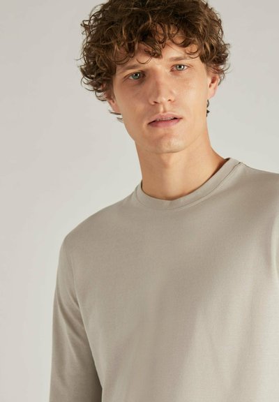 Camisa de manga larga en beige claro con cuello redondo y una textura suave. Diseño sencillo y minimalista sin patrones ni acentos visibles.