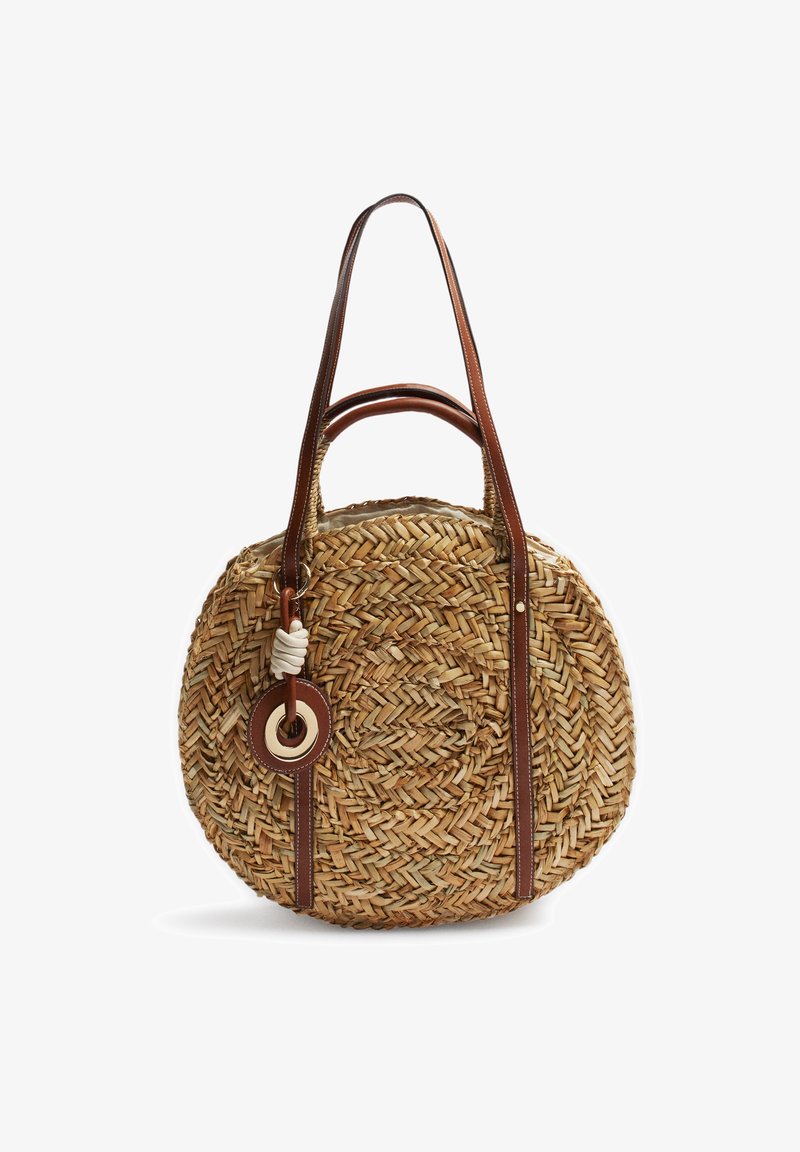 Sac à main rond en paille tissée avec deux poignées en cuir marron et un détail décoratif d’anneau et de nœud sur une sangle.