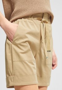 Beiget shortsit, joissa on joustava vyötärönauha ja sivutaskut. Varustettu solmittavalla vyöllä ja käärittyillä lahkeensuilla rentoa istuvuutta varten. Sileä pinta.