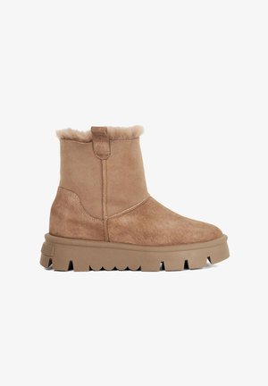 Tan suede ankle boots with a shearling lining, rounded toe, and a thick, textured rubber sole featuring scalloped edges.