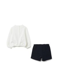 Maglia bianca a maniche lunghe con maniche a sbuffo e bottoni sulla schiena, abbinata a pantaloncini blu scuro testurizzati con vita elastica.