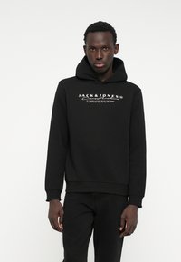 Hoodie noir en tissu doux, avec un logo et un texte blancs bien visibles sur la poitrine. Il a un design classique à enfiler et une capuche avec cordon.