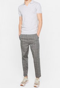 Camisa polo de manga corta en gris claro con cuello en V, combinada con pantalones de cuadros grises y zapatillas multicolores. Presenta un diseño ajustado.