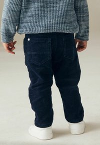 Pantaloni in velluto a coste blu navy con tasche posteriori, abbinati a un maglione azzurro chiaro a coste e sneakers bianche, mostrati da dietro.