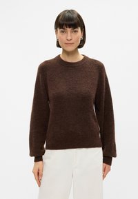 Καφέ πουλόβερ πλεκτό με στρογγυλή λαιμόκοψη, μακριά μανίκια και ριμπ μανσέτα. Το υφασμα έχει υφή που προσδίδει μια απαλή εμφάνιση.