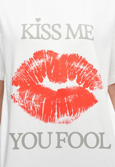 Λευκό βαμβακερό μπλουζάκι με έντονο κόκκινο αποτύπωμα χειλιών και το κείμενο "ΦΙΛΗΣΕ ΜΕ ΗΛΙΘΙΕ" σε γκρι πάνω και κάτω από τα χείλη.