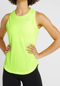 Neon gul atletisk linne med rund hals och tonalt logga. Har en texturerad tyg och en rundad nederkant. Bärs med svarta leggings.