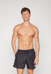 Shorts de bain noirs en tissu léger, dotés d'une taille élastique avec cordon de serrage et d'un logo blanc en bas à droite.