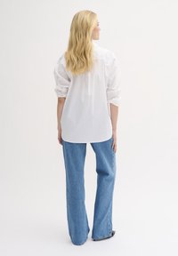 Hvid skjorte med knapper og opstillede ærmer, parret med lyseblå vide ben jeans. Simpel design, bomuldsmateriale og afslappet pasform.