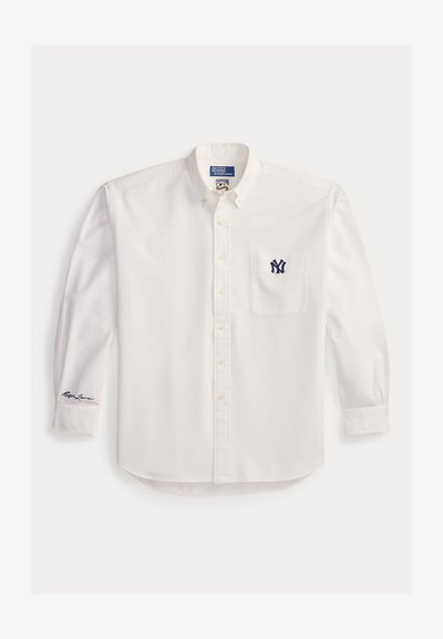Weißes, langärmliges Hemd mit Knopfleiste, Knopfkragen, navyblauem NY-Logo auf der Brusttasche und Ralph-Lauren-Signatur am linken Manschetten Ende.