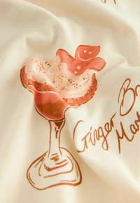 Beige fabric featuring a printed illustration of a dessert glass with a gingerbread man and swirls of cream, accented in warm orange tones.