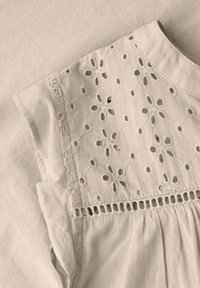Vêtement en coton beige avec motif floral brodé en œillet sur la partie supérieure de la poitrine et manches courtes volantées.