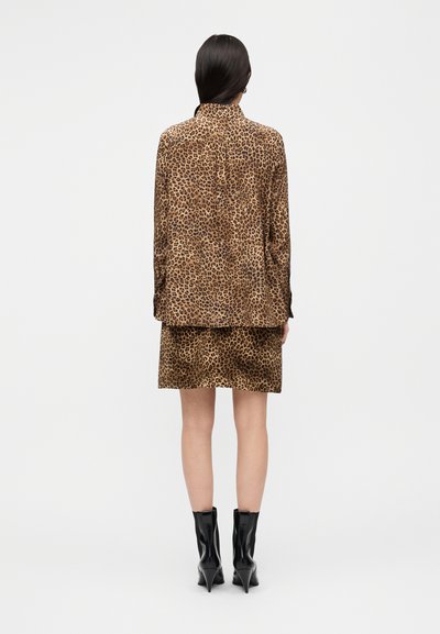 Σετ πουκάμισο και φούστα με λεοπάρ σχέδιο σε καφέ και ταμπά χρώματα. Κατασκευασμένα από λείο ύφασμα, με μακριά μανίκια, συνοδευόμενα από μαύρες μπότες με τακούνι.