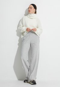 Vit ribbad tröja med hög krage, tillsammans med grå vida sweatsbyxor. Skorna har svarta och beiga designaccenter.