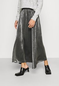 Metallisk silver maxi kjol med en plisserad design, matchad med svarta texturerade klackskor med blockklack. Stickad grå tröja ovanför midjan.