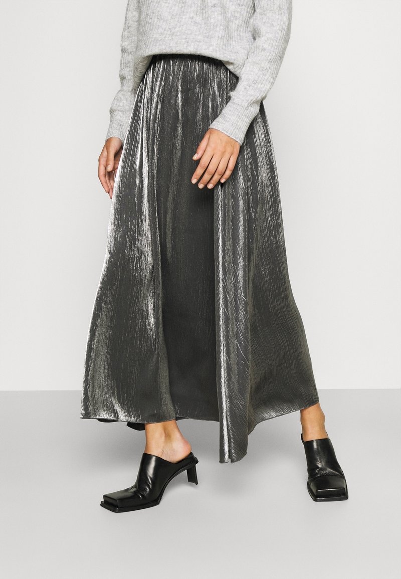 Metallisk silver maxi kjol med en plisserad design, matchad med svarta texturerade klackskor med blockklack. Stickad grå tröja ovanför midjan.