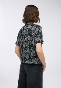 Maglietta nera a maniche corte con motivo paisley bianco, tessuto testurizzato, design accorciato e colletto. Indossata con jeans scuri a vita alta.