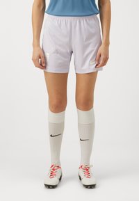 Shorts de football violet clair avec une taille élastique, logo Nike, chaussettes blanches jusqu'aux genoux et chaussures de football teintées de rouge avec des crampons noirs.