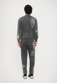 Siva jopa in ujemajoče hlače iz mehke tkanine, z belimi grafikami pajkove mreže in besedilom na rokavih in nogah.