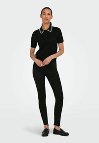 Černé polo tričko s krátkým rukávem a ribbed texturou, doplněné o kontrastní hrotný límec, v kombinaci s černými skinny džínami a černými mokasíny.