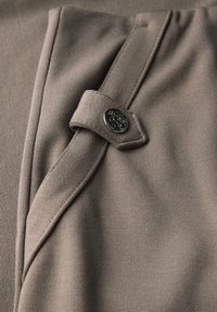 Tissu marron avec un tricot texturé, doté d'un rabat sécurisé par un bouton métallique rond, mettant en valeur ses lignes épurées et son design ajusté.