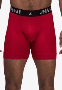 Røde bomulds boxer shorts med en sort elastisk talje, der har "JORDAN" og et logo. Designet er tætsiddende med en glat tekstur og uden mønstre.