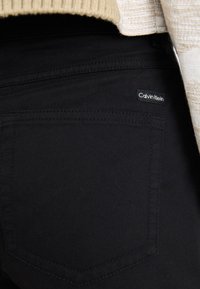 Mustad denim teksad, millel on sile tekstuur, tagapool taskul Calvin Kleini logo ja peened õmblused.