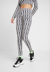 Svarta och vita leggings med ett upprepande textmönster. Tillverkade av stretchigt material, med hög midja och en tajt passform, tillsammans med svarta skor.