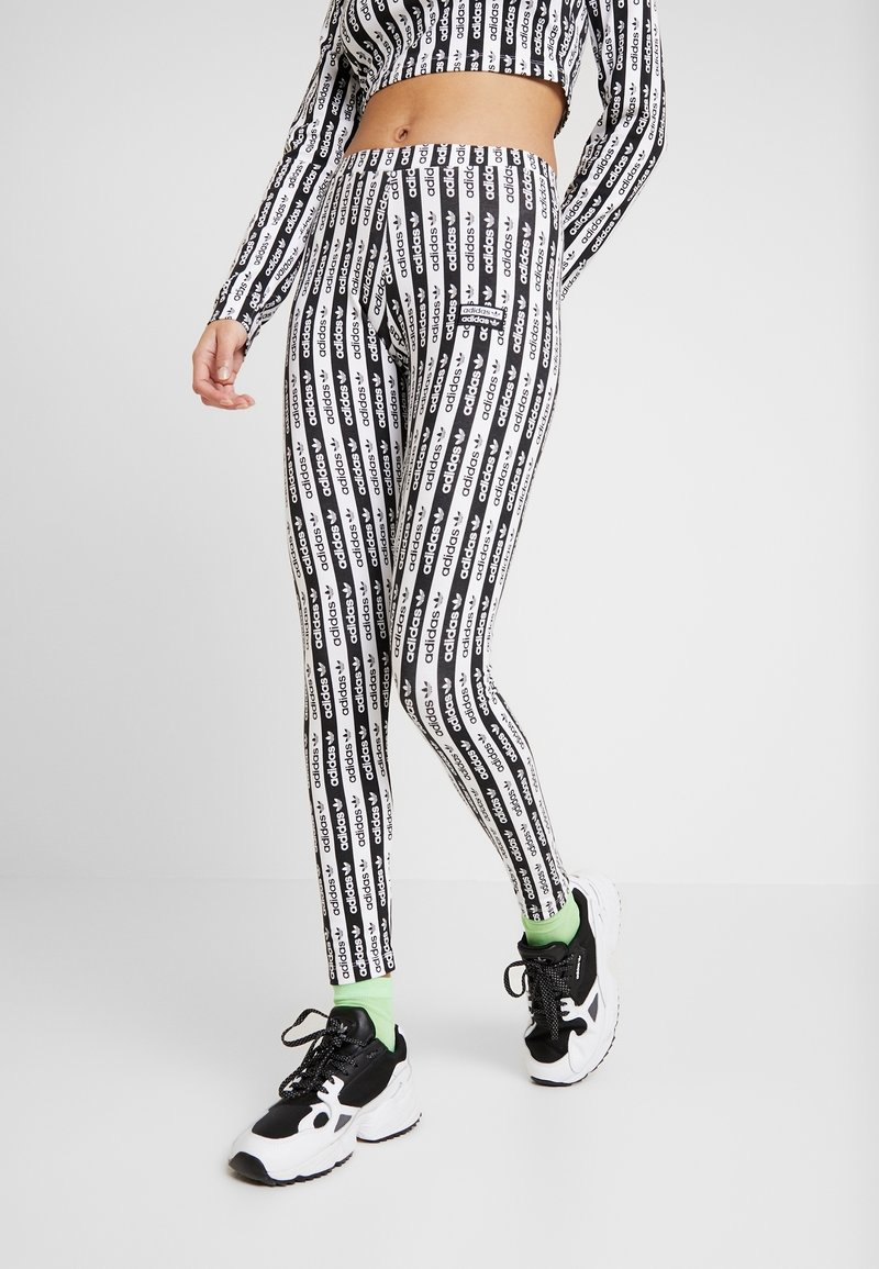 Svarta och vita leggings med ett upprepande textmönster. Tillverkade av stretchigt material, med hög midja och en tajt passform, tillsammans med svarta skor.