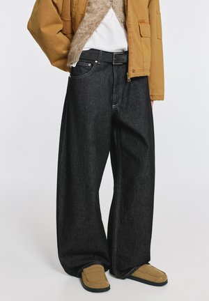 Čierne široké džínsy z denimu s vysokým pásom, klasickými vreckami a kontrastným bielym šitím. Kombinované s béžovou bundou a obuvou.