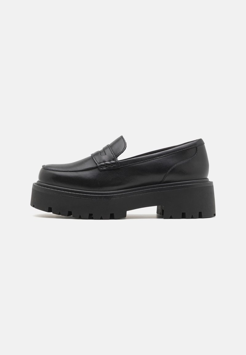 Mocassin en cuir noir avec semelle crantée épaisse et petit talon, présentant une bande décorative sur le dessus, vu de profil sur fond blanc.