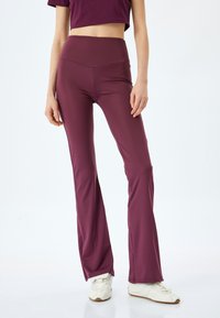Bordeaux flare leggings met een hoge tailleband, gemaakt van rekbare stof; gecombineerd met witte sportschoenen en een cropped top in een bijpassende kleur.
