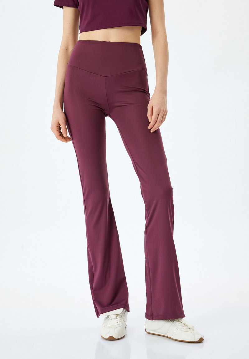 Bordeaux flare leggings met een hoge tailleband, gemaakt van rekbare stof; gecombineerd met witte sportschoenen en een cropped top in een bijpassende kleur.