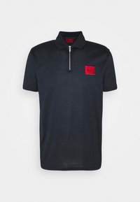 Polo noir à manches courtes avec une fermeture éclair frontale argentée et un patch rectangulaire rouge sur la poitrine gauche portant l'inscription "HUGO".