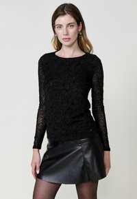 Top nero a maniche lunghe con motivo floreale, realizzato in materiale trasparente; abbinato a una minigonna in pelle nera, caratterizzata da una texture liscia.