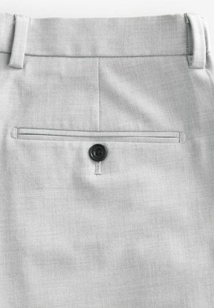 Pantalones gris claro con tela texturizada, que cuentan con un bolsillo trasero con un cierre de botón negro y un diseño de pliegue rectangular.