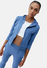 Ljusblå zip-up hoodie med en figursydd design, mjuk textur och fickor som en kenguru, tillsammans med matchande figursydda byxor.