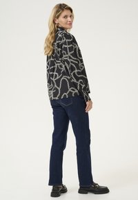 Camicia nera a maniche lunghe con un motivo a catena bianca, abbinata a jeans dritti blu scuro e scarpe con zeppa nere.