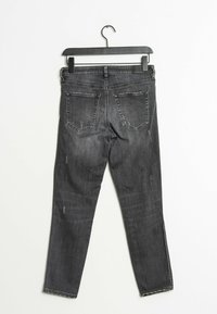 Jean slim fit en negro deslavado con bolsillos traseros colgados de una percha negra sobre un fondo blanco.