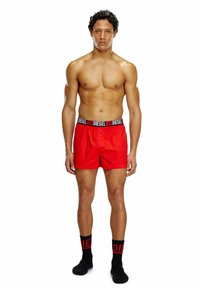 Rode boxershorts met een zwarte merkband. Model staat, draagt zwarte sokken met rode letters. Spaanse stof, casual pasvorm.