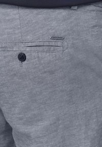 Pantalons gris clair en tissu texturé, dotés d'un unique bouton à la taille, d'une poche arrière et d'une petite étiquette de logo.